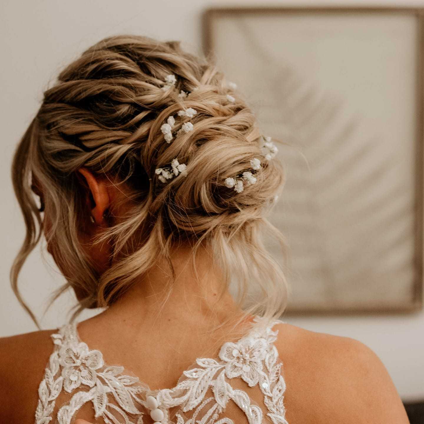 Woman with elegant updo hairstyle adorned with white floral accessories, wearing lace detailed dress.