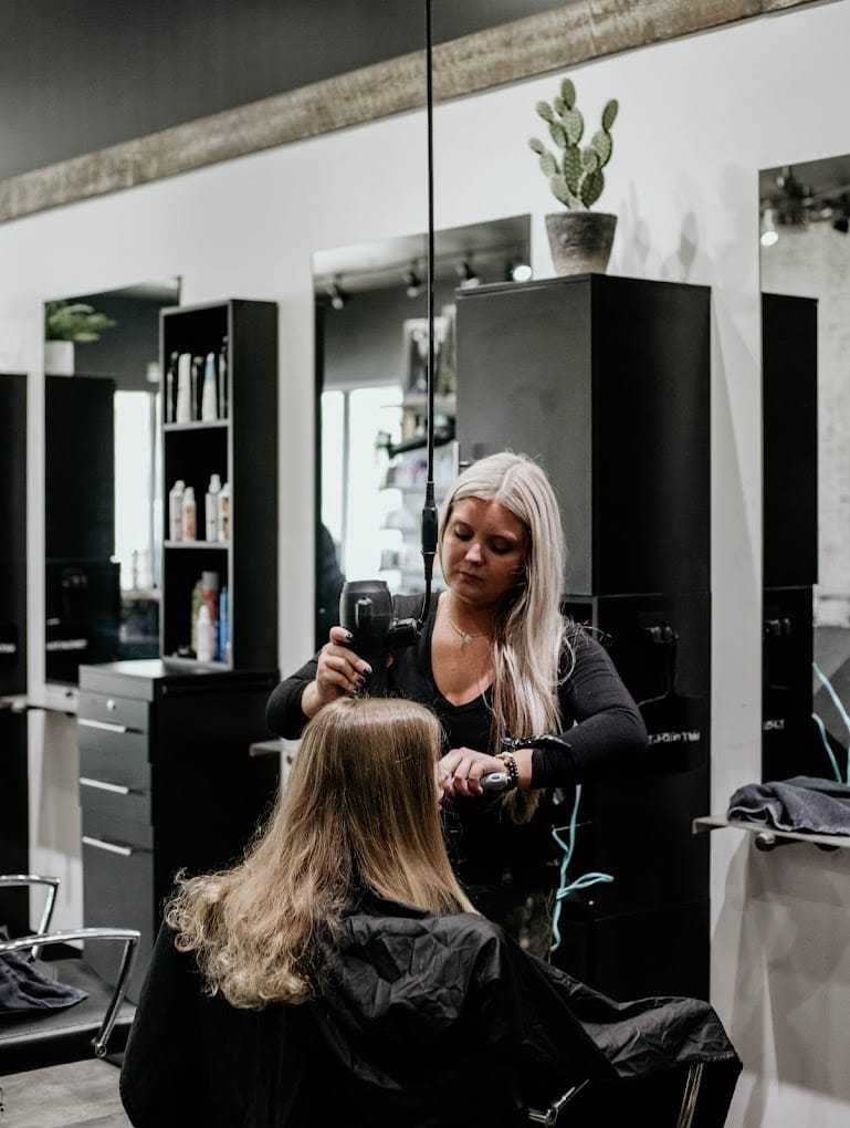 Hairstylist blow-drying a client's long hair in a modern salon.